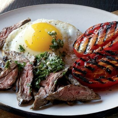 A plated breakfast of steak, fried egg and grilled tomato