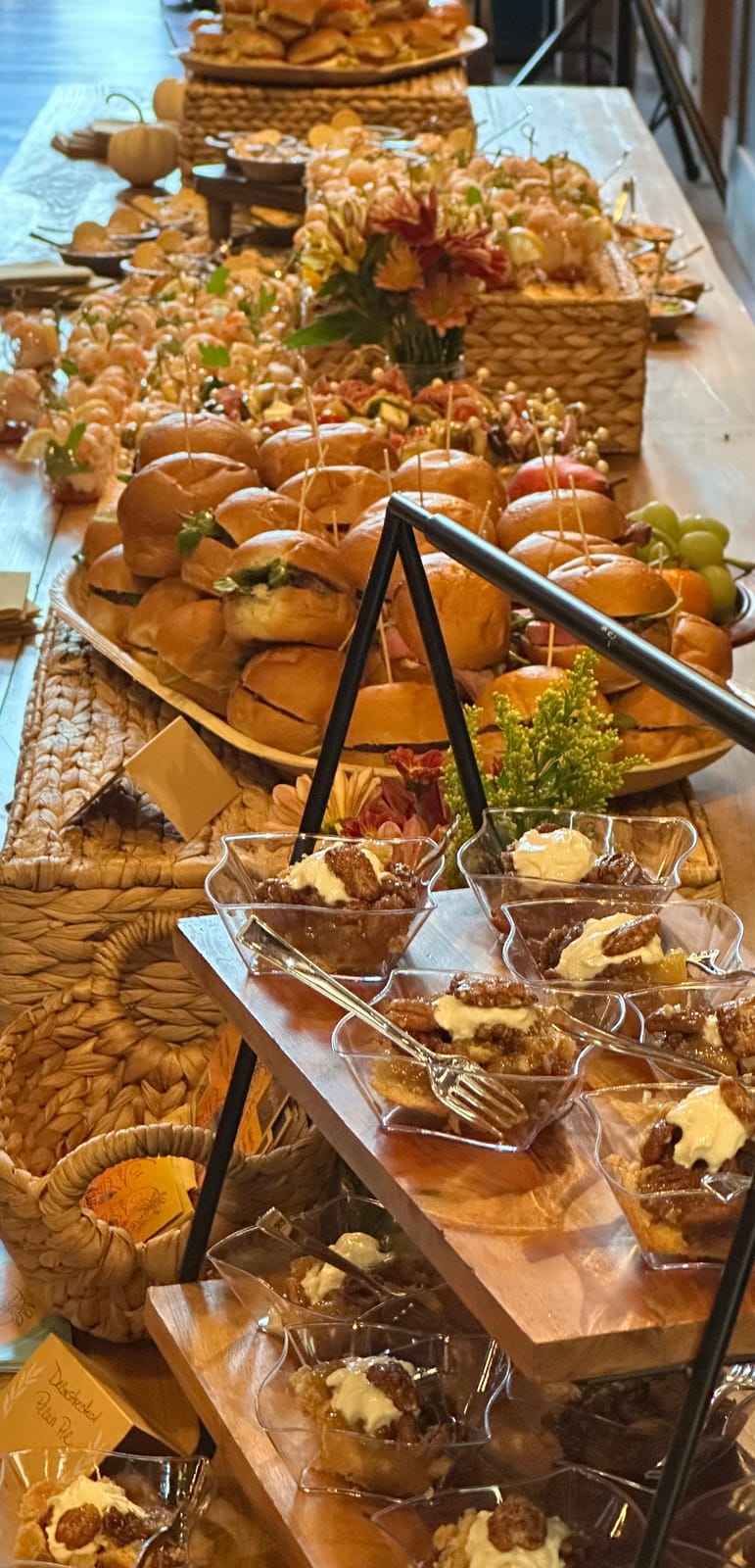A lush Nibbles N Bites grazing table styled with sliders, seasonal fruit, dessert cups and flowers